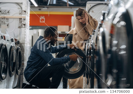 Sitting and opening. Man and woman are choosing washing machine in the store Sitting and opening. Man and woman are choosing washing machine in the store 134706000
