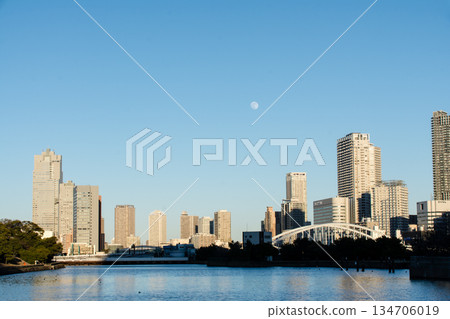 The vast waters of Tokyo Bay near Odaiba under the clear blue sky and moonlit daytime skyline, with Tokyo's skyscrapers visible in the distance The vast waters of Tokyo Bay near Odaiba under the clear blue sky and moonlit daytime skyline, with Tokyo's skyscrapers visible in the distance 134706019