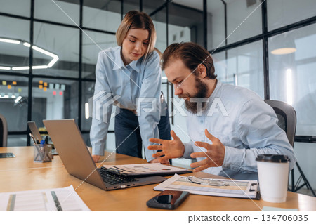 Guy is angry, reading document. Man and woman are in the office together 134706035