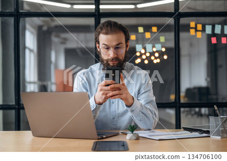 Black smartphone in hands, sitting. Businessman is working in the office Black smartphone in hands, sitting. Businessman is working in the office 134706100