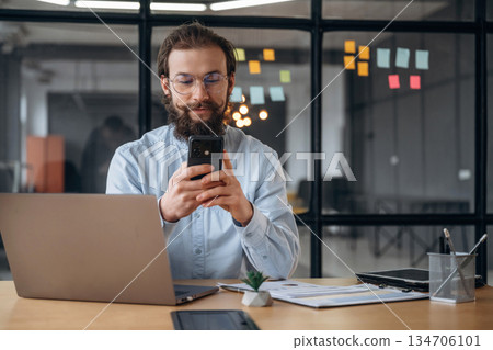 Cheerful facial expression, holding phone. Businessman is working in the office Cheerful facial expression, holding phone. Businessman is working in the office 134706101