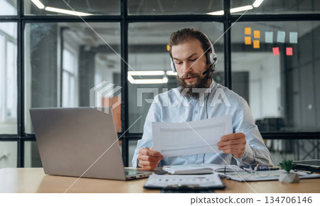 Sitting in headphones, online conference. Businessman is working in the office Sitting in headphones, online conference. Businessman is working in the office 134706146