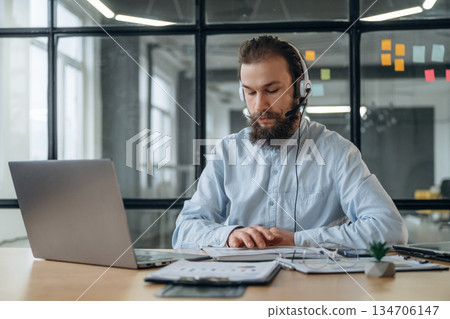 Sitting in headphones, online conference. Businessman is working in the office Sitting in headphones, online conference. Businessman is working in the office 134706147