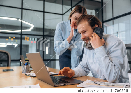 Whispers advices, talking by phone. Man and woman are in the office together Whispers advices, talking by phone. Man and woman are in the office together 134706236