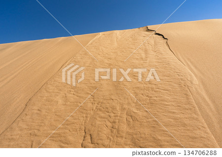 Bottom view of sand dune slope under clear blue sky, textured sand ridges 134706288