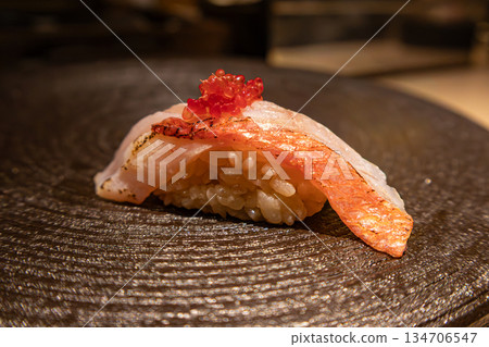 壽司櫃檯上的一份壽司:炙烤白魚,上面放著鮭魚籽 壽司櫃檯上的一份壽司:炙烤白魚,上面放著鮭魚籽 134706547