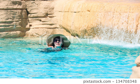 A girl in a hat stands neck-deep in pool water 134708348