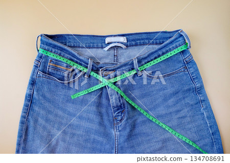 Blue jeans with measuring tape on color background. Blue jeans with measuring tape on color background. 134708691