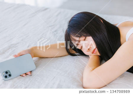 A young woman lying in bed and looking at her smartphone 134708989