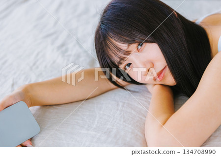 一位年輕女子躺在床上看著她的智慧型手機 134708990