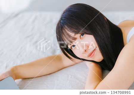 一位年輕女子躺在床上看著她的智慧型手機 134708991