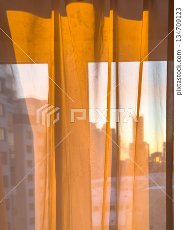 Golden sunrise through sheer curtains in urban apartment Golden sunrise through sheer curtains in urban apartment 134709123