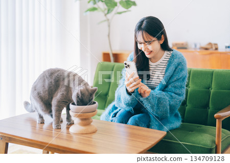 A woman takes a photo of a cat eating food A woman takes a photo of a cat eating food 134709128