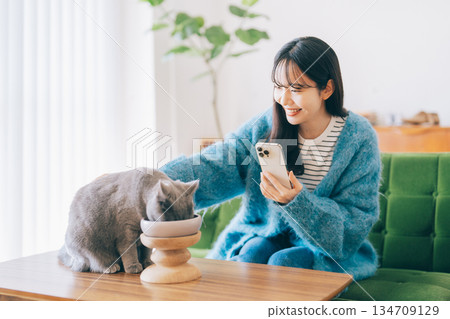 A woman takes a photo of a cat eating food A woman takes a photo of a cat eating food 134709129