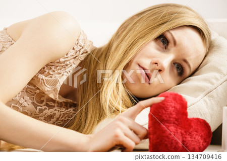 Sad woman holding red pillow in heart shape 134709416