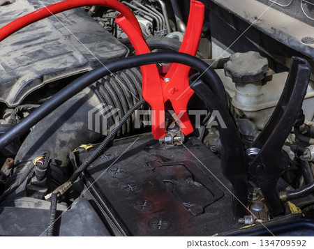 Close-up of car charger cable jump starting a dead car battery. Black and red charging cable clamps on a battery terminals for charging, car repair and maintenance concept. 134709592