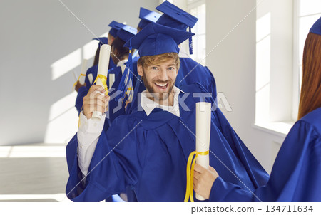 Graduate Man in Cap and Gown Holds Diploma Amidst Fellow Students Graduate Man in Cap and Gown Holds Diploma Amidst Fellow Students 134711634
