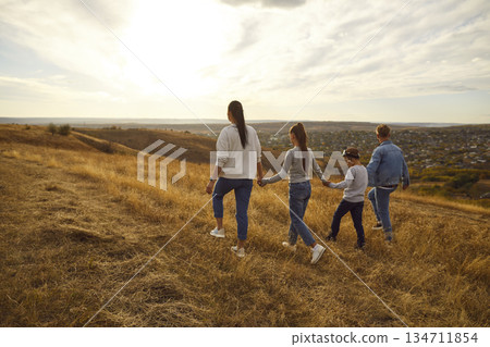 Back view of family holding hands and walking on field during sunset, spending free time outdoors Back view of family holding hands and walking on field during sunset, spending free time outdoors 134711854