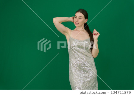 gorgeous woman in a silver shiny dress on a green background chromakey sexuality femininity sensuality . Concept themes of fashion, luxury, elegance, and evening events. 134711879