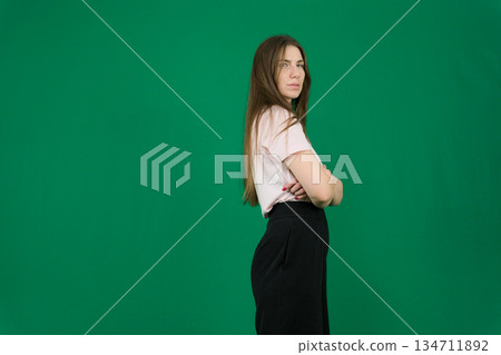 portrait of a beautiful, happy, neat woman in a beige turtleneck sweater and black-rimmed glasses, standing on a light background sideways to the camera and crossing her arms over her chest 134711892