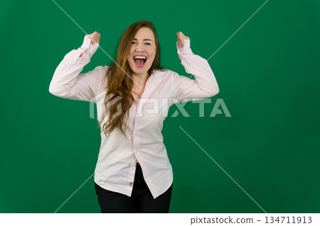 Joyful young Asian woman in a brown shirt holding smartphone with happy successful expression, isolated by white background. 134711913