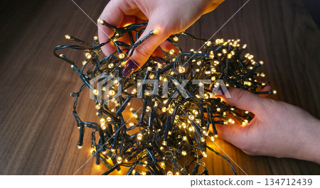 Untangling the Christmas garland. A Christmas garland with glowing lights. New Year's decoration. High quality photo Untangling the Christmas garland. A Christmas garland with glowing lights. New Year's decoration. High quality photo 134712439