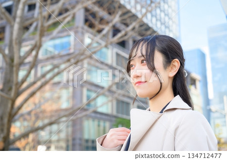 A fresh-faced businesswoman in her 20s wearing a suit and smiling in a building district A fresh-faced businesswoman in her 20s wearing a suit and smiling in a building district 134712477
