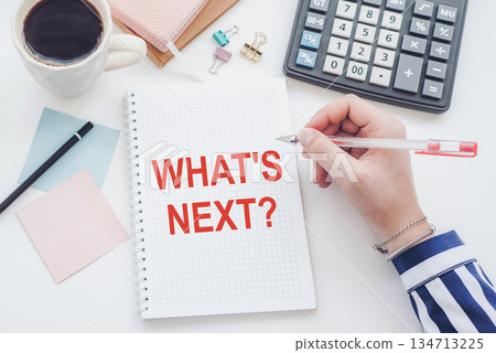 A hand writing a question What's next on a notebook. A hand writing a question What's next on a notebook. 134713225
