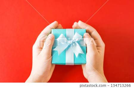 Child's hands holding turquoise gift box on red background Child's hands holding turquoise gift box on red background 134713266