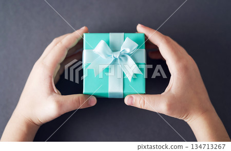 Child's hands holding turquoise gift box on gray background Child's hands holding turquoise gift box on gray background 134713267