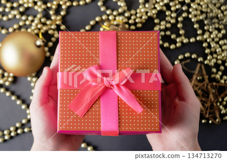 Children's hands are holding a red gift box on a Christmas background. Children's hands are holding a red gift box on a Christmas background. 134713270