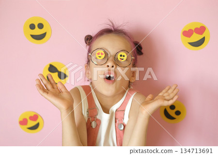 A surprised girl in glasses with emoji icons pasted on the lenses. World Smile Face and Social Media Day 134713691