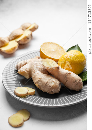 Fresh ginger root and lemon on ceramic plate with leaves on light background. 134713803