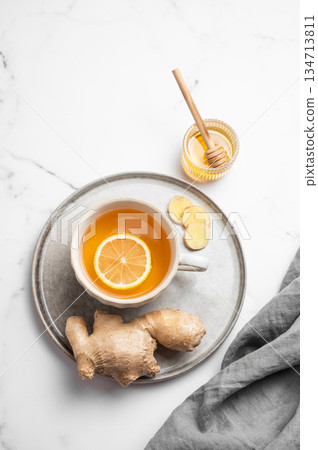 A cup of hot tea with fresh lemon and ginger on a plate on a light marble background 134713811