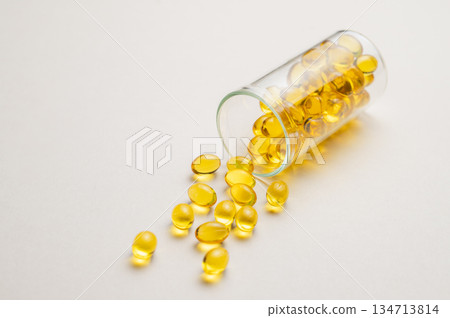 Yellow softgel vitamins capsules scattered in a bottle on a light background close up. Yellow softgel vitamins capsules scattered in a bottle on a light background close up. 134713814
