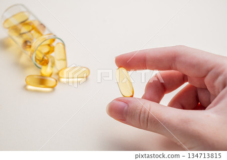 A hand holding a soft capsule containing Omega on a yellow background. A hand holding a soft capsule containing Omega on a yellow background. 134713815