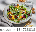 A fresh salad of beets, orange, and arugula with feta, walnuts, and balsamic dressing on a plate 134713818