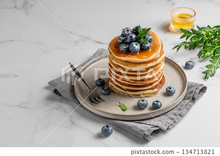 Pancakes with fresh blueberries on a gray plate on a marble background with honey and fresh berries. Pancakes with fresh blueberries on a gray plate on a marble background with honey and fresh berries. 134713821