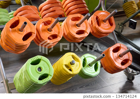 Colorful weight plates organized on a rack in a gym, promoting fitness and strength training. 134714124