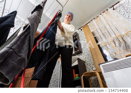 Wet laundry after washing middle aged woman hangs on wire drying rack in bathroom. 134714408