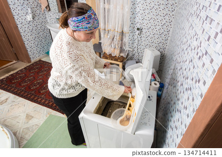 Woman pours laundry powder into compartment of vertical washing machine. Woman pours laundry powder into compartment of vertical washing machine. 134714411