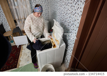 Iron rich water left rusty stains on plastic of vertical washing machine, woman over 50 loads clothes into drum. Iron rich water left rusty stains on plastic of vertical washing machine, woman over 50 loads clothes into drum. 134714415