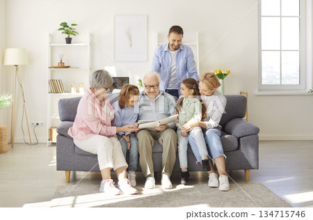 Happy family unit, old grandparents, parents and small children watching photo album to remember  134715746