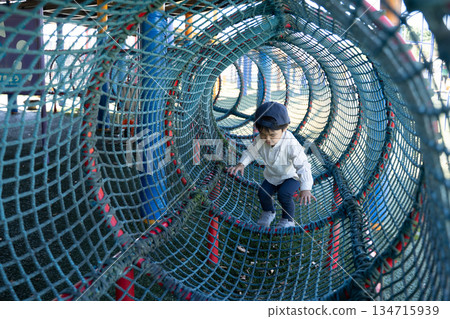 Boy playing on mesh tunnel playground equipment Boy playing on mesh tunnel playground equipment 134715939