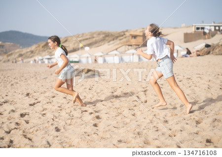 Playful girls running on sandy beach during summer 134716108