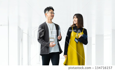 兩名商人,一男一女,邊走邊聊,穿過辦公室。 兩名商人,一男一女,邊走邊聊,穿過辦公室。 134716157