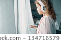 Child listening to music on headphones at home near window 134716579