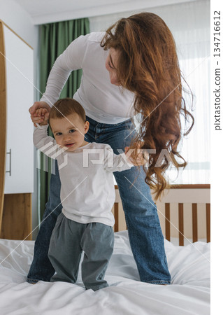 Young mother playing with her baby at home, enjoying a warm and cozy family moment full of tenderness, comfort, natural light, and playful parent-child connection. 134716612