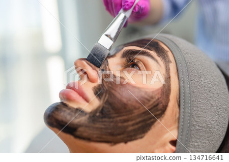 Applying a carbon mask on a woman face with a brush during a carbon laser facial preparation in a beauty clinic. Applying a carbon mask on a woman face with a brush during a carbon laser facial preparation in a beauty clinic. 134716641