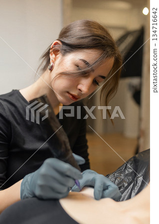 tattoo artist working on a woman chest design in a studio, showing the process of professional tattooing, precision, sterile gloves and cosmetic procedure atmosphere. tattoo artist working on a woman chest design in a studio, showing the process of professional tattooing, precision, sterile gloves and cosmetic procedure atmosphere. 134716642